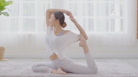 Side view of Asian woman doing Yoga exercise,Yoga One Legged King Pigeon pose or Eka Pada Rajakapotasana.Calm of healthy young woman breath deep and meditation with yoga at home.Positive Self Care