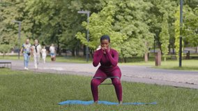 Athletic African black girl in sportswear exercising, performs squats with rubber band. Attractive focused biracial young woman doing stretching during morning workout in park. Pilates, yoga, fitness - Powered by Shutterstock - Get 15% off with code: PIKWIZARD15