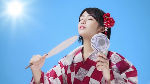 Young asian woman with a kimono using a handy fan and a neck fan. Portable electric fan.