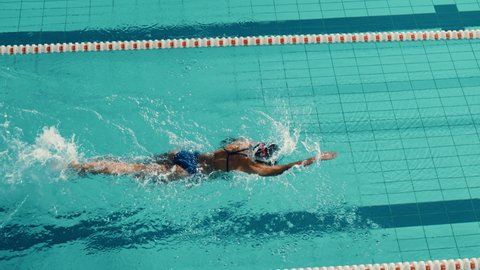 Beautiful Female Swimmer Using Front Crawl, Freestyle in Swimming Pool. Professional Athlete Training to Win Championship. Cinematic Slow Motion, Stylish Colors, Artistic High Angle Tracking Shot