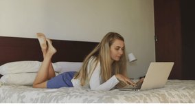 Animation of network social media icons over smiling relaxing on bed using laptop. social media and global communication interface technology concept digitally generated video.