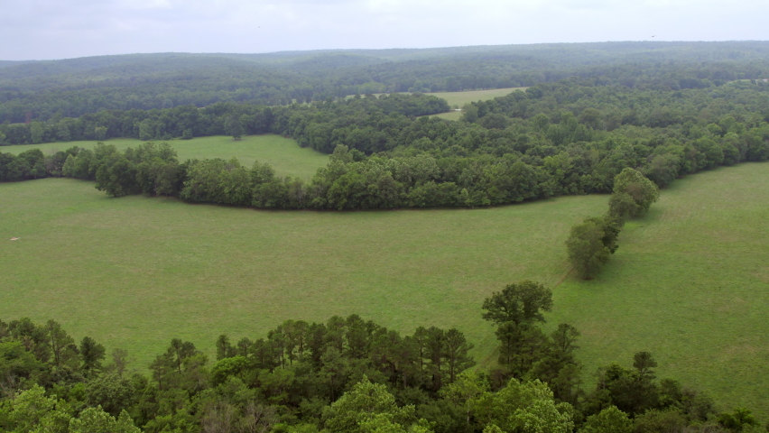 Aerial flyover fields and trees in southern Missouri on a cloudy summer day.