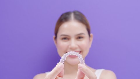 Young smiling woman holding Invisalign braces in studio, dental healthcare and Orthodontic concept.	