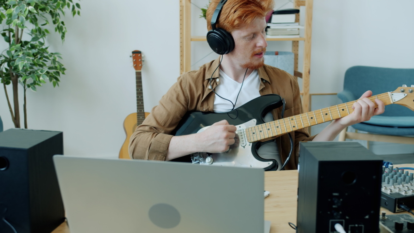 Slow motion of attractive young musician playing guitar and singing having fun indoors in apartment. Happy people and professional instruments concept.