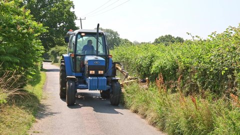 Much Hadham, Hertfordshire. UK. July 20th 2021. Man in a tractor using a flail to mow grass verges in a country Lane