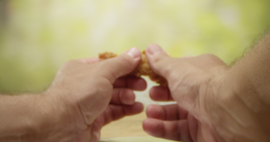 Male Hands Shred a Slice of Fried Chicken Strip in Two Pieces on a Kitchen Table with Dolly Pushing in Royalty-Free Stock Footage #1076260169