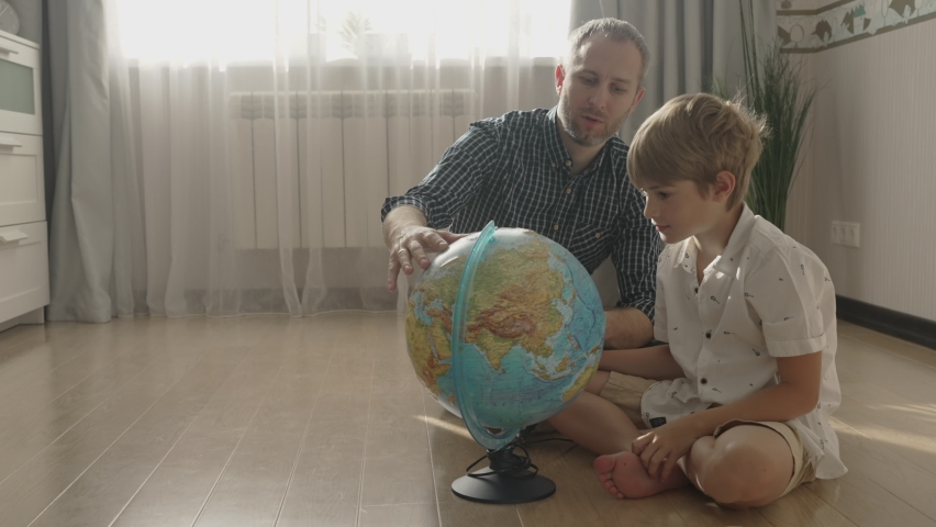 Happy dad and small kid boy looking at globe, exploring new countries for travel, playing, enjoying time together at home. Smiling father having fun with cute child son in living room.