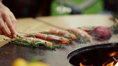 Closeup unknown woman putting herbs on bbq grill outdoors. Shrimp frying on grill with herbs on backyard. Unrecognizable woman preparing food for bbq party outside. Healthy food cooking outdoor