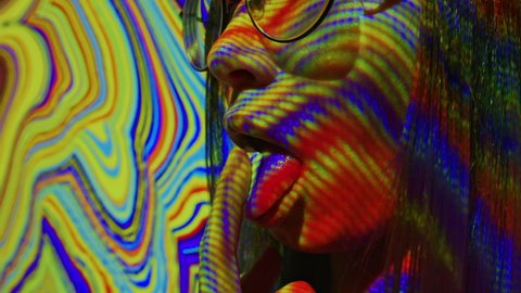 A young woman puts a lsd acid blotter on her tongue. Multicolored psychedelic abstract background. The concept of psychedelia, nirvana and addiction