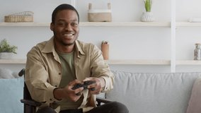 Joyful Disabled African American Man Playing Videogame And Shaking Fists Winning Game Sitting In Wheelchair At Home. Joy Of Victory. Wheel Chair Lifestyle And Leisure Concept. Zoom In