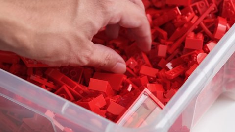 Tambov, Russian Federation - July 13, 2021 A person digging through a pile of red lego bricks in big plastic container to find the ones he wants