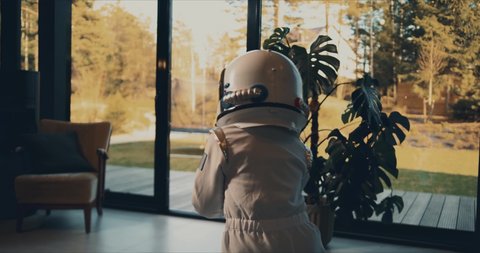 Camera follows little kid run out of house with dog to terrace trampoline wearing white astronaut space suit and helmet.