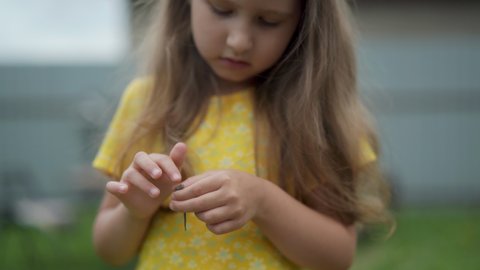 little curious girl of 5 years old, holding a small lizard on her hand, while in the fresh air. The child looks at the amphibious animal with curiosity and interest. The baby strokes the lizard