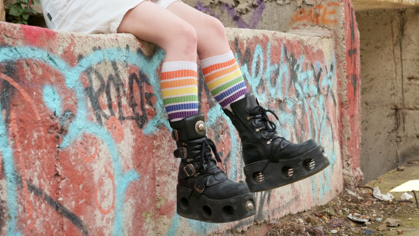 Teenager girl slide with rough boots striped stockings sits on ornate wall of an abandoned building Slow motion. Alternative in youth. An alternative in youth. Hipster, freak, emo, grunge, LGBT Royalty-Free Stock Footage #1076278904