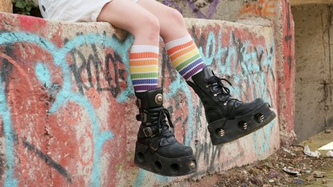 Teenager girl slide with rough boots striped stockings sits on ornate wall of an abandoned building Slow motion. Alternative in youth. An alternative in youth. Hipster, freak, emo, grunge, LGBT