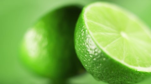 The fresh limes are rotating slowly on bright green background. Concept of fruit vitamins and healthy food. Close up.
