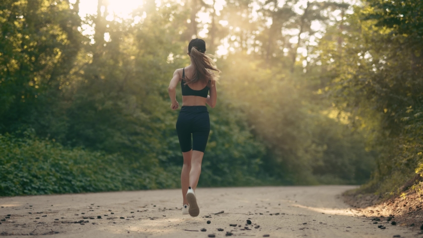 A young woman runner is listening to music in earphones and training in summer forest. The fitness girl is jogging outdoor. Concept of workouts running and healthy lifestyle. Slow motion. Royalty-Free Stock Footage #1076280011
