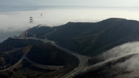 Cinematic Aerial drone footage of heavy fog pouring over the hills and surrounding the Golden Gate Bridge in San Francisco, California, USA
