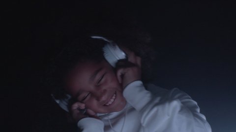Portrait of smiling african american kid girl listening modern music melody wearing headphones, dancing indoor close up. Trendy sound enjoyment, funny activity, happy relax using cool audio technology