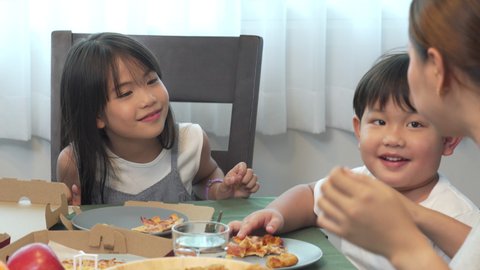 Happy Asian family parents with little daughter and son eating fried chicken and pizza for dinner together. Father and mother with child boy and girl enjoy eating and sharing a meal together at home.
