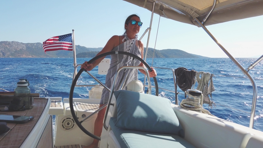 Summer holiday sailing concept: Female sailor navigating sailing yacht over blue Aegean sea. Nautical travel on luxury boat. Confident and stylish young woman captain driving a ship. Holding a wheel Royalty-Free Stock Footage #1076300684