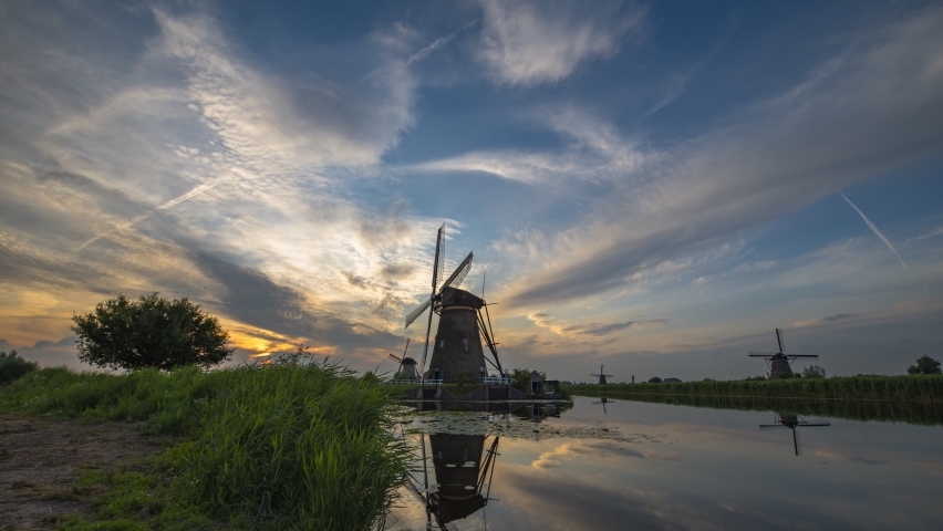 Timelapse of a sunset and clouds moving above old dutch windmills and a river in Kinderdijk, Netherlands. 4K UHD video.