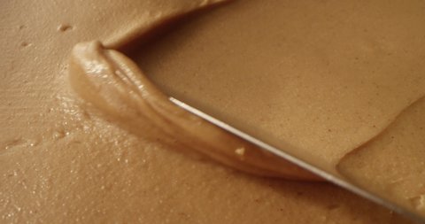 Peanut Butter Spreading with a Knife Creating Creamy Caramel Color Background a Macro Shot