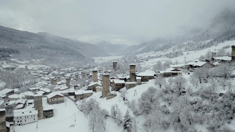 This is an aerial drone camera shot of Mestia village in Svaneti region, Georgia, Caucasus mountains. Shot taken on a cloudy winter day. Svan defence houses – towers covered in snow.