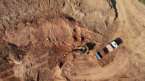 Excavator load the sand into dump truck. Aerial view of an backhoe on earthworks. Open pit development and sand mining. Loader digging ground for foundation pit. Earthmoving at construction site. 
