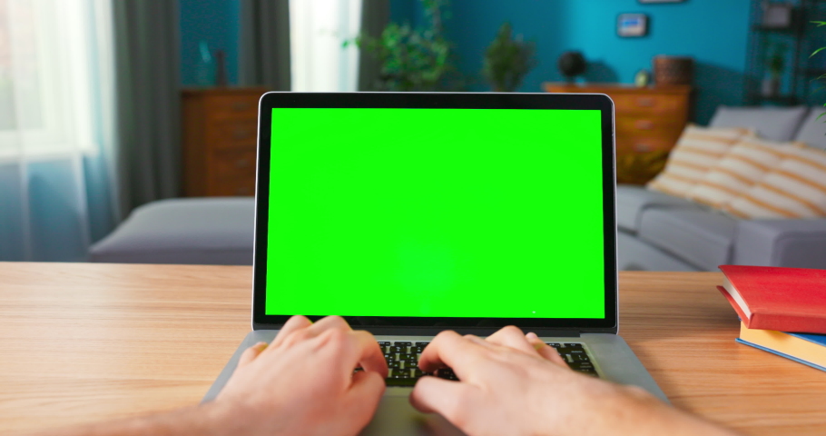 Shot of male Hands Typing on a keyboard laptop with blank screen. Zoom out On a Modern Personal Computer with Mock-up Green Screen Display Standing on the Desk of the Cozy Home Office. Royalty-Free Stock Footage #1076305844