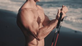 Close up video of strong pectoral and biceps muscles works with elastic band. Six-pack torso bodybuilder do workout at the sea shore. Concept of health and beauty. High quality 4k footage