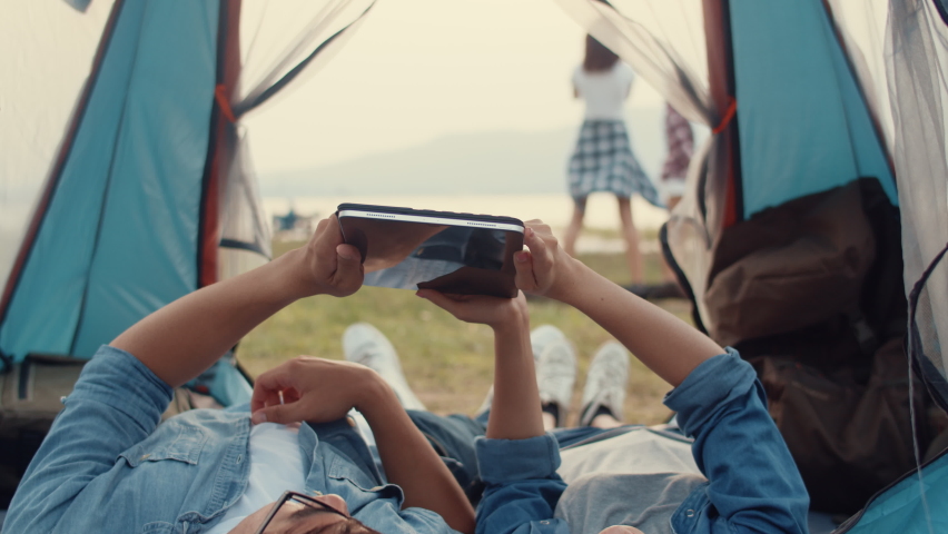 Couple Asia teenagers have relax time look photo album on tablet with happy moment togetherness in national park campsite. On background beautiful nature, mountains and lake. Travel blogger concept.