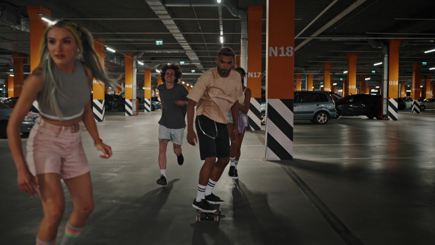 Urban tricks. Company of happy young diverse friends having fun at underground parking, riding skateboards and jumping together, slow motion Royalty-Free Stock Footage #1076308562