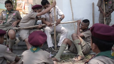 Sai Khao Pattani, Thailand, March 18, 2016: Thai Boy Scout activities group of secondary school students boys in uniform making wooden catapult teacher shows how to join sticks tie with a rope