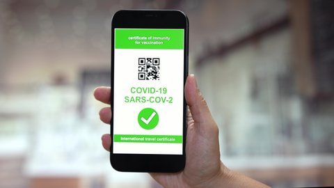 A person holding a smartphone with the Vaccine Passport green card for Coronavirus Covid-19 Sars-cov-2 on the monitor and showing it to the camera.