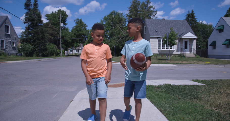Two young african american boys playing football while walking to school on the sidewalk in a residential neighbourhood