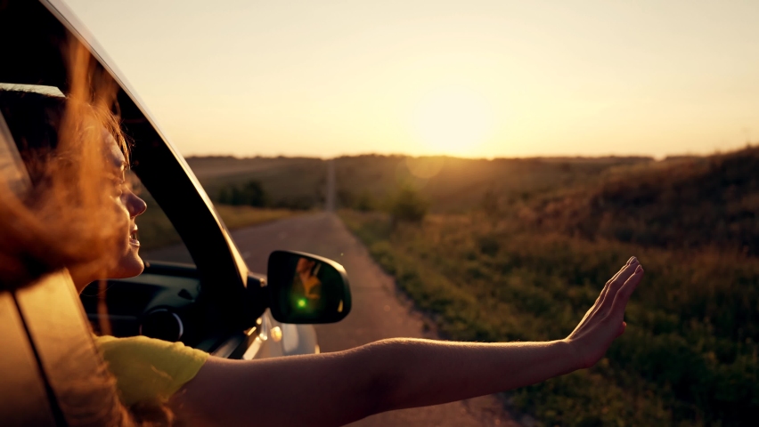 Happy girl in car window. Hair in wind. Girl travels by car. Hand in sun. Windy breeze from car window. Happy girl smiling from car window. Windy breeze in your hair. Hand in the rays of the sun | Shutterstock HD Video #1076317790