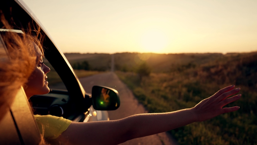 Happy girl in car window. Hair in wind. Girl travels by car. Hand in sun. Windy breeze from car window. Happy girl smiling from car window. Windy breeze in your hair. Hand in the rays of the sun Royalty-Free Stock Footage #1076317790