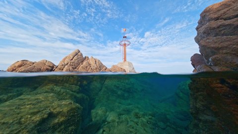 Split-shot, over-under shot. Stunning video of half underwater half sky with rocks ad a red navigational mark. Liscia Ruja, Costa Smeralda, Sardinia, Italy.