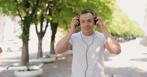 Smiling man puts on big headphones walking in the summer city, slow motion 4k at 120fps