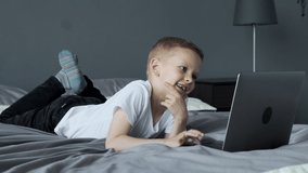 A Small Child Uses A Computer, Looks at The Laptop Screen, Watches Videos or Cartoons, Lies on the Sofa in a Bright Room At Home