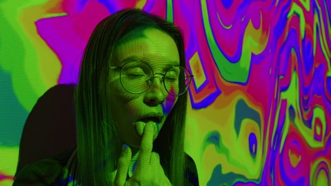 A young woman puts a lsd acid blotter on her tongue. Multicolored psychedelic abstract background. The concept of psychedelia, nirvana and addiction