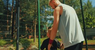 Basketball player father raising up son on hands, helping boy scoring hoop on basketball court outdoors in sunlight