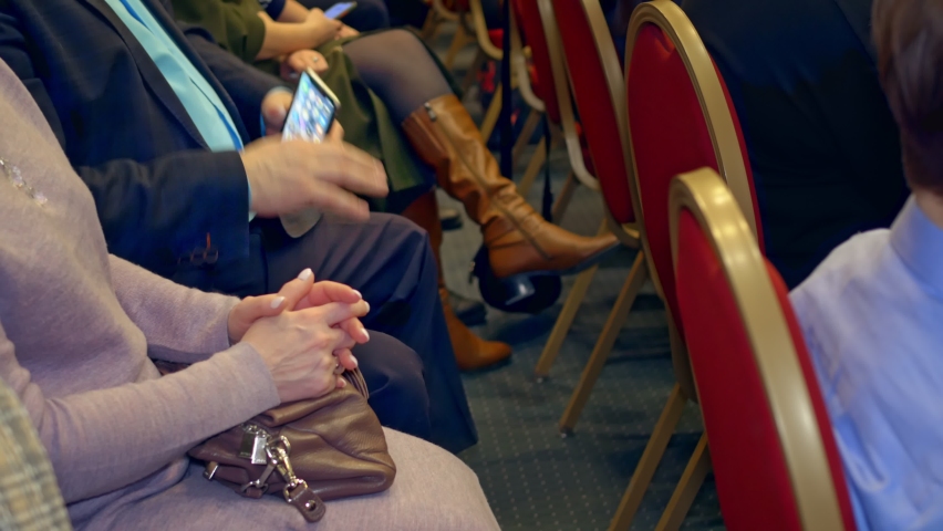 Lovers of fashion shows gathered in the hall, sat on red, comfortable seats. They are waiting for the start of the fashion show. The man scrolls across the smartphone screen.