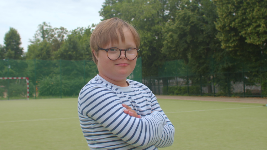 Portrait smiling boy on football field. Children Down syndrome disease resulting from genetic abnormality in which extra chromosome in human body. Correction of vision glasses. Healthy life children. Royalty-Free Stock Footage #1076335361