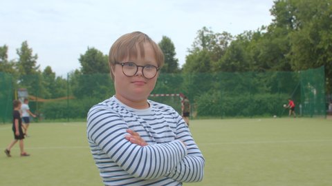 Portrait smiling boy on football field. Children Down syndrome disease resulting from genetic abnormality in which extra chromosome appears in human body. Correction of vision glasses.