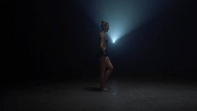 Flexible woman doing handstand with splitted legs indoors. Young female gymnast training in dark studio. Athletic girl practicing rhythmic gymnastics in spotlight background.