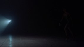 Young woman gymnast dancing in spotlight background. Graceful sportswoman jumping in dark space. Slim girl doing rhythmic gymnastics indoors. 