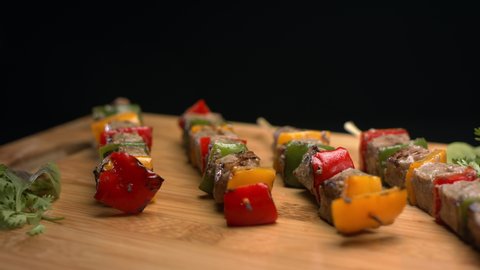 Cooked delicious meat skewers with pieces of bell pepper on wood board are rotating slowly. Close-up view of skewers on a black background. Food concept. Asian food