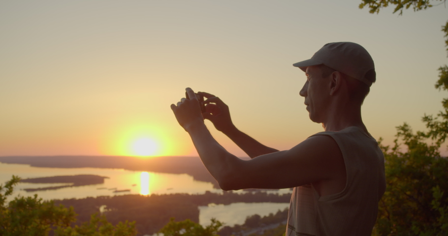 A lone traveler on the top of a mountain takes pictures of the valley with his phone. Man makes photos of nature on a smartphone.